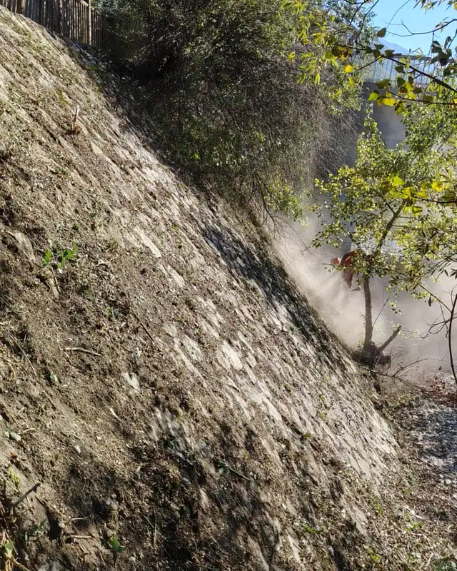 Talus en pente en cours de débroussaillage, poussière soulevée par la débroussailleuse